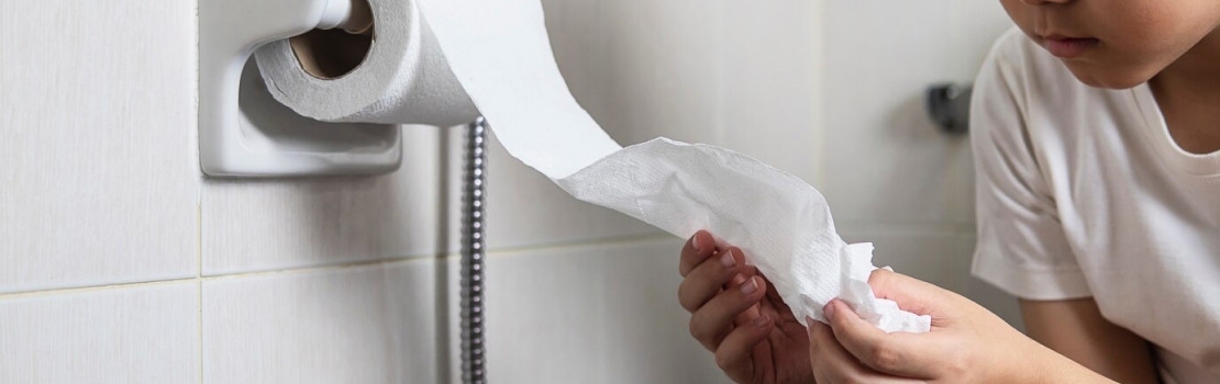 Dieťa s bolesťou brucha sediace na posteli, znázorňujúce príznaky hnačky u detí.